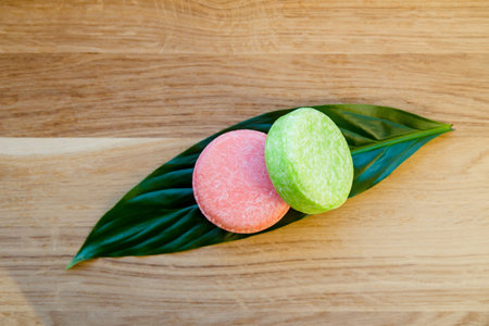 Pink and green color solid shampoo bars or conditioner bar on green leaf on wooden background. Minimalist beauty set indoors, copy space.の写真素材