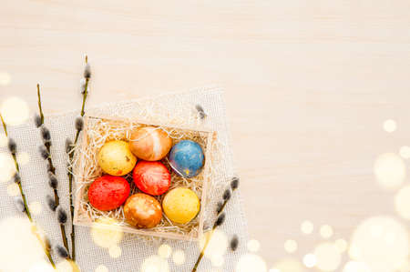 Flat lay view of colorful gold leaf colored Easter eggs in wood shred nest with pussy willow branches for decoration, lot of copy space on beige wood background. Easter background lot of copy space.の写真素材
