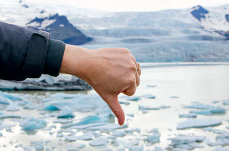 Person hand showing thumb down emotion towards climate change and global worming. Melting glacier on...