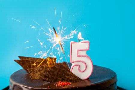 Number 5 birthday candle burning and sparkler with sparks fly on cake. The fifth birthday or anniversary celebration concept. Lot of copy space on blue background.の写真素材