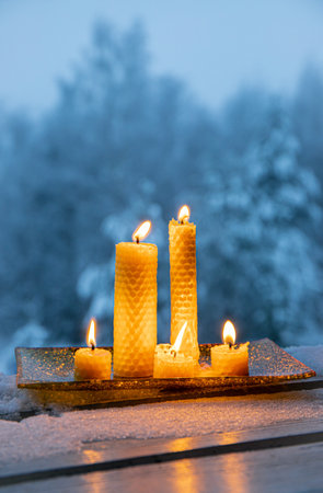 Set of natural rolled beeswax candles from pressed beeswax honeycomb sheet at home balcony outdoors snowy winter forest on background. Hobby concept. Lot of candles burning with coの写真素材