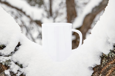 White blank coffee mug mock up template. Cozy seasonal products advertisement background. Single cup on snowy Scandinavian winter nature background. Room for text.の写真素材
