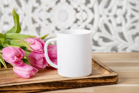 Selective focus on single one white mug mock up. Cup on home table with decorative spring flowers on background and bohemian style wood panel. Cozy seasonal products advertisementの写真素材