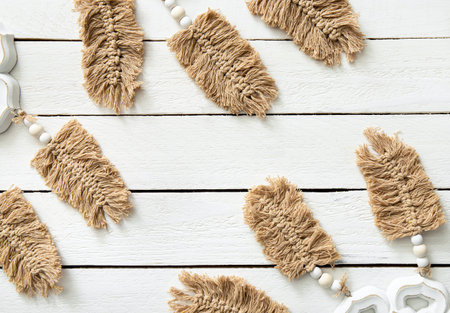 Light brown leaf or feather shape macrame hanging against white wood board background in home room....