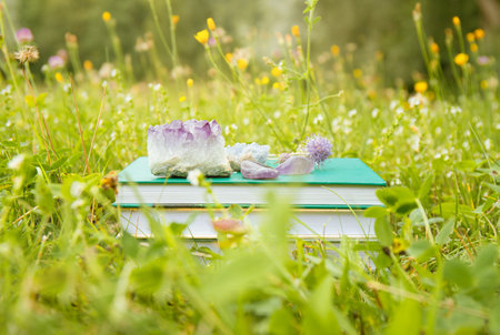 Self help or esoteric theme books in stack with crystal geodes outdoors in sunny summer day with blokeh nature meadow garden on background.の写真素材