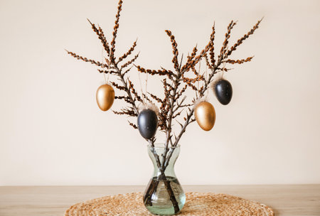 Tree branches in vase with colored Easter eggs hanging on string. Nice warm beige earthly tones. Minimal home Easter decoration.の写真素材