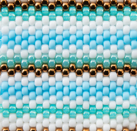 Macro shot of boho style beading backdrop. White, blue and bronze color beading striped pattern.