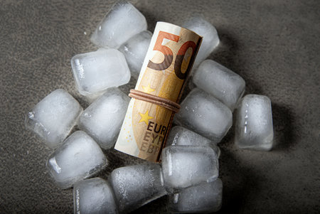Concept of freezing the funds. Above view of Euro money roll inside ice cubes on gray studio background. Copy space.の写真素材