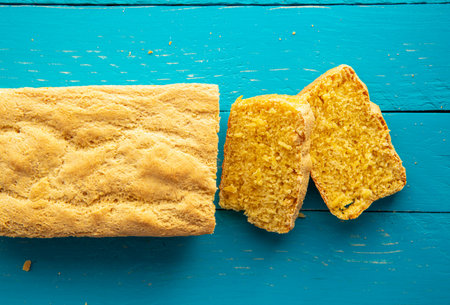 Beautiful homemade yellow sliced cornbread loaf on blue wood board background. Above view, rustic look.の写真素材