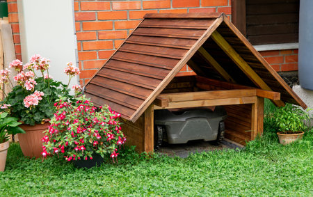 Robot lawn mower inside homemade wooden lawn mower garage outdoors in summer in home garden.の写真素材