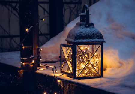 Black metal candle lantern with led lights sting inside in the winter outdoors. Snowy wood patio in the night, during Christmas holidays.の写真素材