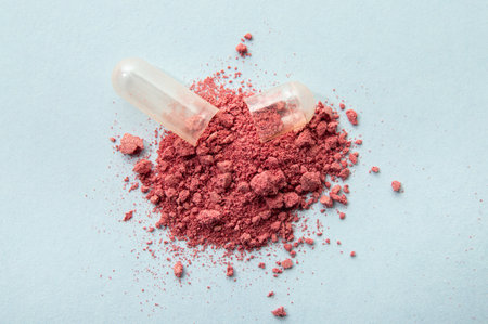 Opened cranberry Vaccinium Oxycoccus gel capsule with red vitamin powder spilled out. Blue studio background.の写真素材