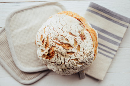Loaf of homemade sourdough bread in home kitchen on white wood background.