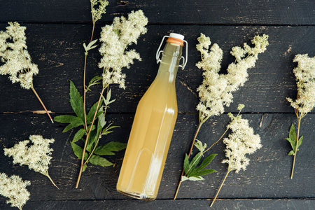 Flat lay view of homemade Meadowsweet Filipendula ulmaria flowers syrup bottle and picked...