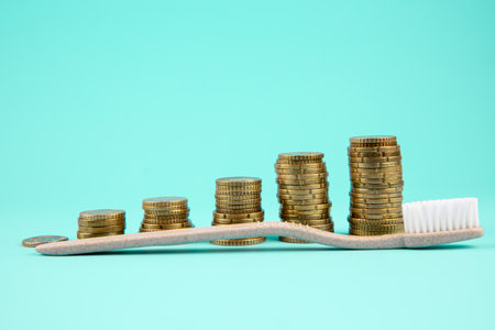 Concept of dental costs increasing. Stacks of coins lined up in ascending order with a beige toothbrush placed diagonally on top of them. Studio shot. Rising diagonally upwards.の写真素材
