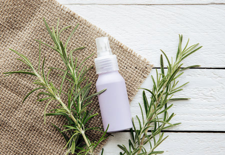 Homemade rosemary Salvia rosmarinus water made from rosemary leaves, for hair and skin care. A purple spray bottle between rosemary branches on white rustic wood board background.の写真素材