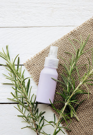 Homemade rosemary Salvia rosmarinus water made from rosemary leaves, for hair and skin care. A purple spray bottle between rosemary branches on white rustic wood board background.の写真素材