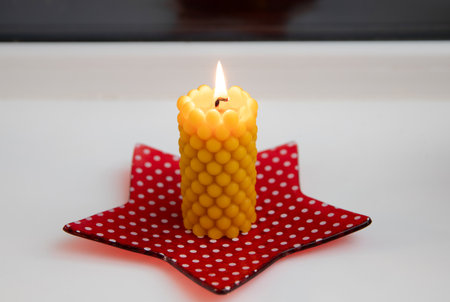 A beeswax candle with a bubbly shape, cast in a handmade silicone mold, burns on a windowsill at home in dark.の写真素材