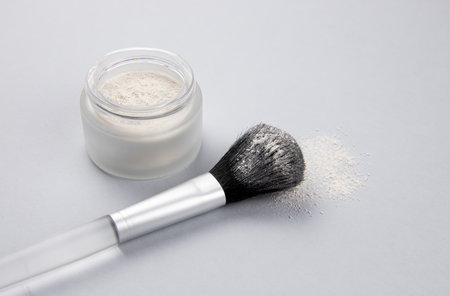 Side view of homemade dry powder shampoo with cinnamon in a matte glass jar, with apply make up brush on gray color background.の写真素材