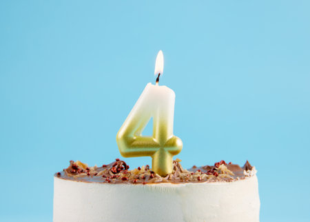 Number 4 birthday candle burning on cake. The fourth birthday or anniversary celebration concept. Lot of copy space on blue background, studio shot.の写真素材