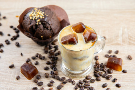 Side view of iced coffee drink in mug, coffee ice cubes scattered on table, decorated with coffee...