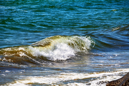 A brilliant green wave breaks near the shore, sparkling in the sunlight. Vivid water colors and...