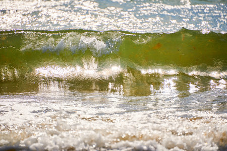 A brilliant green wave breaks near the shore, sparkling in the sunlight. Vivid water colors and...