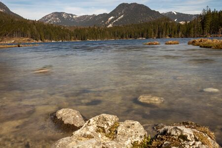 Mountain lake with stones in the foreground and snow on the mountains.の写真素材