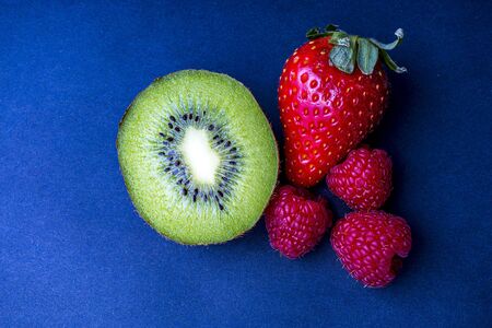 Kiwi, strawberry and two raspberries in a close-up against gray background.の写真素材