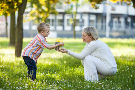 Beautiful boy and mom in spring park with present  Mothers day or birthday celebration conceptの写真素材