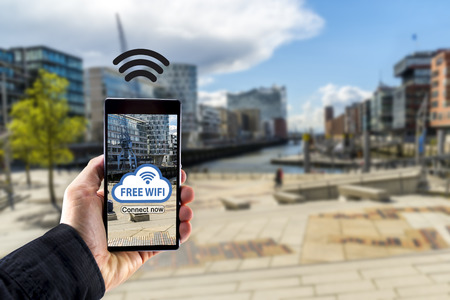 Hand holding smartphone mobile device with city in background - Free wifi connectionの写真素材
