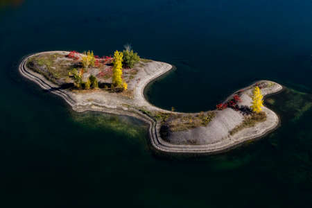 Aerial view of a sandbank island with colorful autumn trees surrounded by blue water