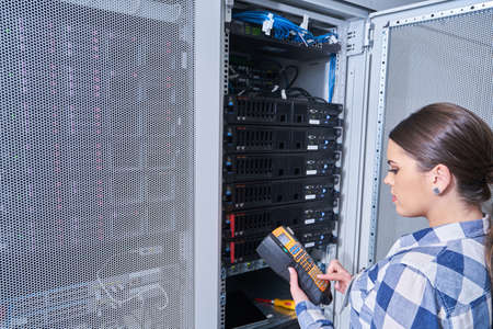 female technician working on server maintenance in white server room next to open server rack