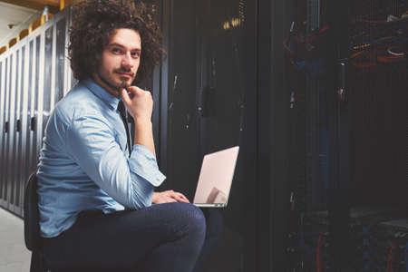 Young technician working on a laptop next to black server racks