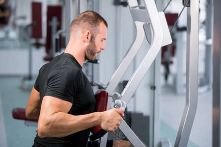 Determined young muscular man working on fitness machine at the gym