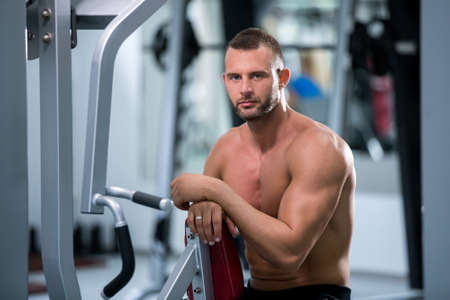 Determined young muscular man working on fitness machine at the gym