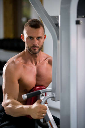 Determined young muscular man working on fitness machine at the gym