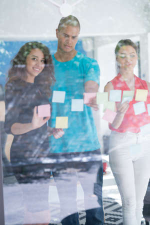 business, startup, planning, management and people concept - happy creative team writing on stickers at office glass boardの写真素材