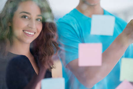 business, startup, planning, management and people concept - happy creative team writing on stickers at office glass boardの写真素材