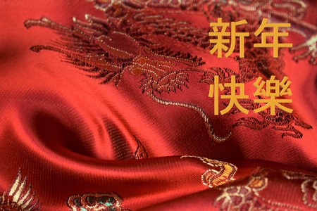 Chinese New Year greeting on an embroidered satin background. Translation: Happy New Year (in...