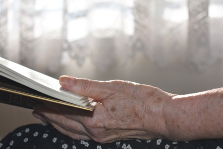 The hand of an old reader woman hold a book in front of a window