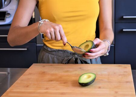 A young woman empty half avocado with a spoon on a wooden boardの写真素材