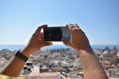 A man tries to take a picture of an urban landscape with his mobile avoiding the reflection of the sunの写真素材