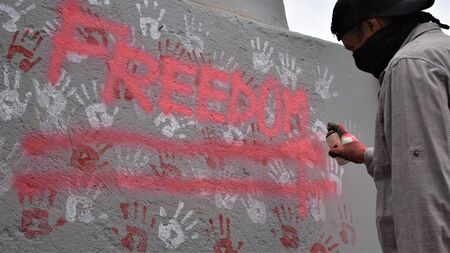 A hooded activist makes a protest graffiti on a wallの写真素材