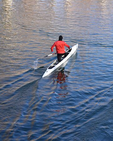 Rear view of an athlete rowing in a kayak over calm waters
