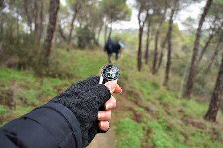 A person consult the route holding a compass in a hand. Detail of the compass and the mittened hand...