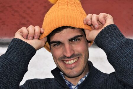 Close-up of a smiling young man putting on a yellow knit bonnetの写真素材