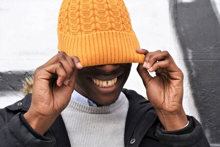 Close-up of an young smiling african man frisking to put himself a yellow knit bonnet