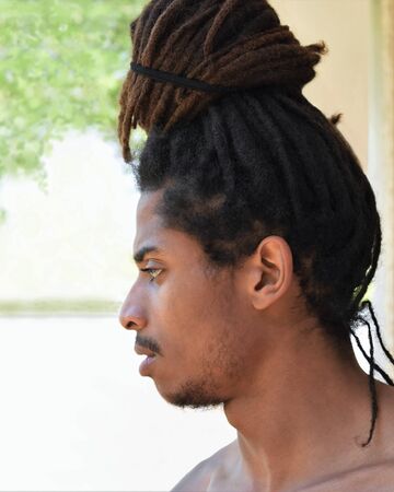 Profile portrait of a meditative African guy with dreadlocks gathered over his head in a bun, isolated on a light backgroundの写真素材