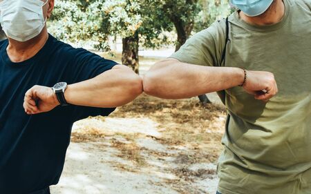 Two friends with facial mask greet each other with the elbow before starting a country walk. New safe greeting rules.の写真素材
